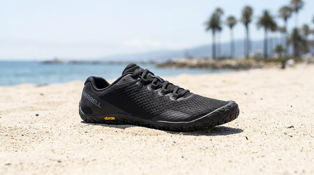 Merrell Vapor Glove 6 sobre arena de playa con palmeras al fondo